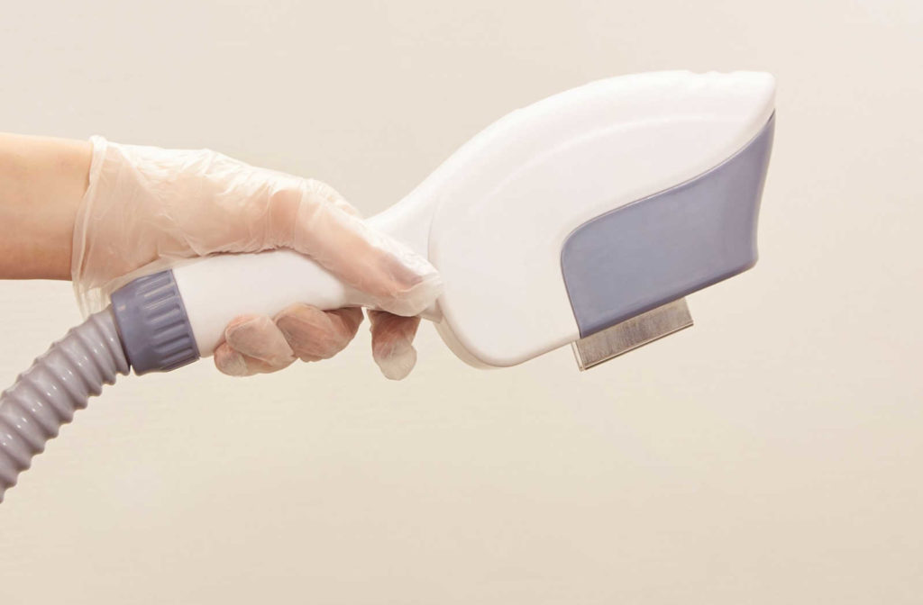A hand wearing a medical glove holds out the handheld device from and IPL machine.