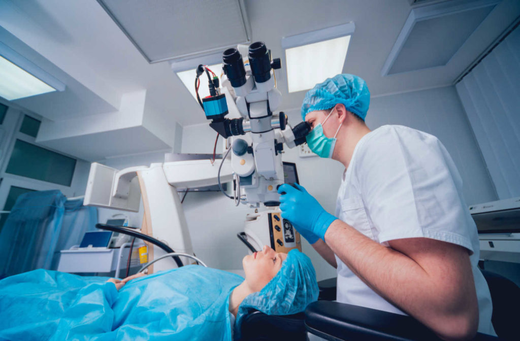 A doctor looking at a patient's eye through a microscope while the patient lays on the exam bed during surgery.