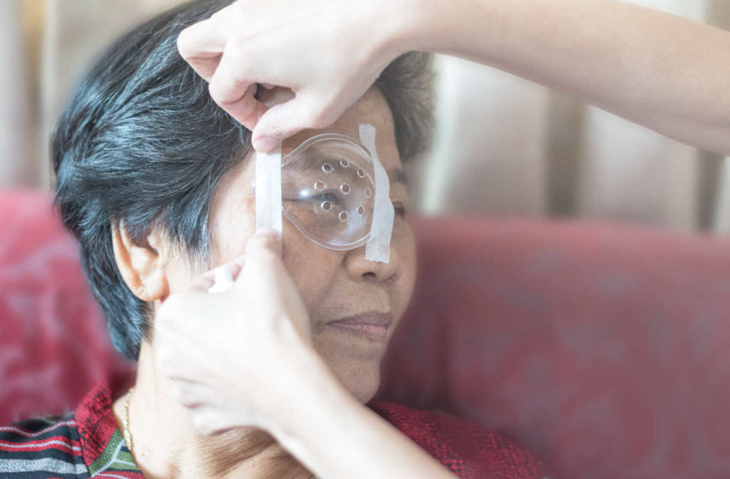 An eye doctor helping an elderly female patient to place an eye shield over her eye after undergoing cataract surgery.