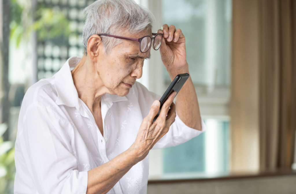 A senior woman with grey hair pushing her glasses up to see the text on her smartphone clearly.