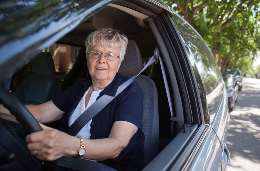 A senior woman wearing glasses with white hair sitting in a vehicle.