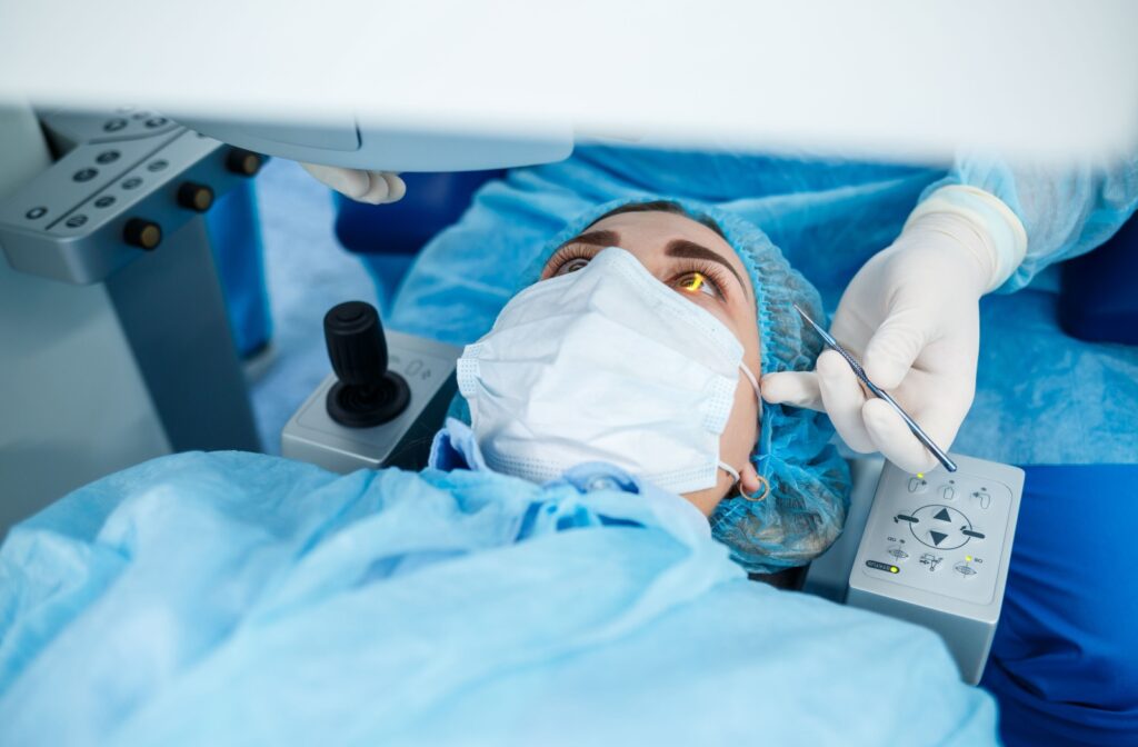 A patient undergoing LASIK surgery lying on a table wearing a blue gown. A doctor in white gloves prepares a surgical instrument.
