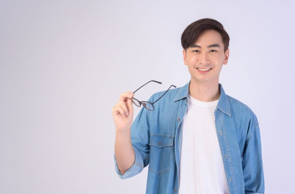 A person smiles while holding their glasses to the side and seeing clearly after LASIK