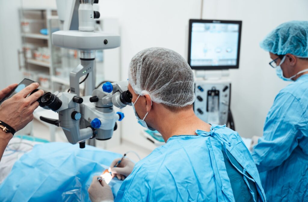View from behind as an ophthalmologist performs eye surgery in blue scrubs and 2 people assist