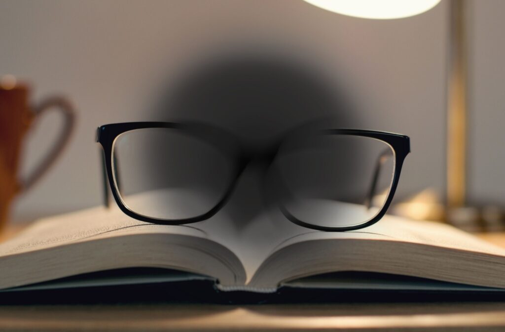 An image of glasses on an open book with a large black spot in the centre that demonstrates vision loss from AMD.